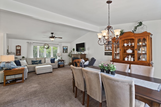 carpeted dining room with ceiling fan with notable chandelier, vaulted ceiling with beams, and a fireplace