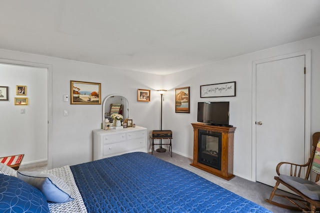 carpeted bedroom featuring a glass covered fireplace and baseboards