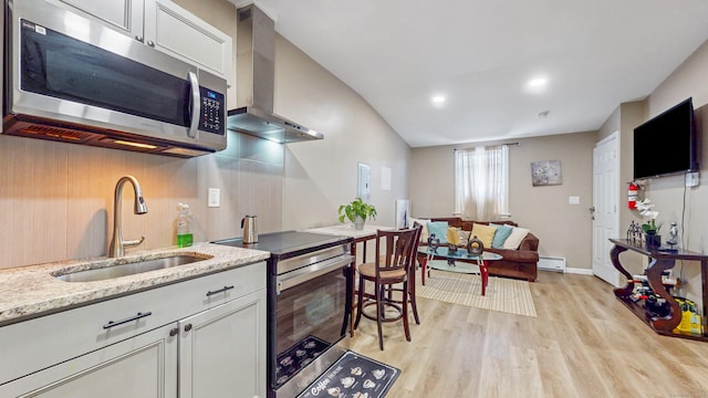 kitchen featuring a sink, stainless steel appliances, wall chimney exhaust hood, light stone counters, and light wood-style flooring