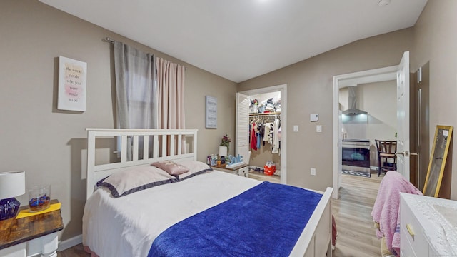 bedroom featuring light wood-style floors, a closet, a walk in closet, vaulted ceiling, and baseboards