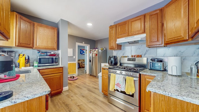 kitchen with tasteful backsplash, light wood-style floors, under cabinet range hood, appliances with stainless steel finishes, and brown cabinets