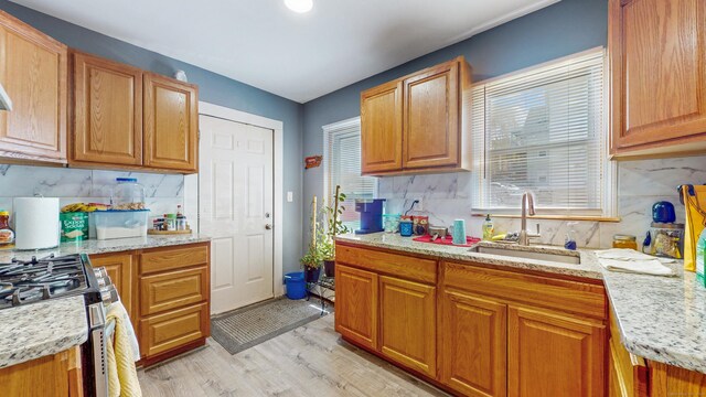 kitchen with stainless steel range with gas cooktop, a sink, tasteful backsplash, and light wood-type flooring
