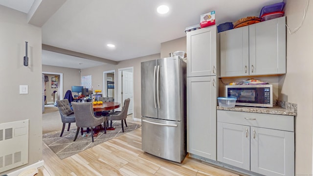 kitchen featuring recessed lighting, light stone counters, stainless steel appliances, light wood finished floors, and open floor plan