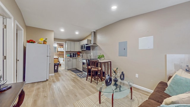 living area with lofted ceiling, light wood-type flooring, electric panel, and baseboards