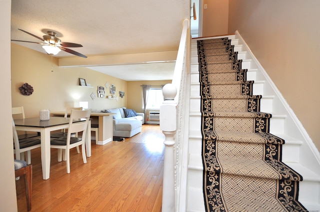 stairway with a ceiling fan, wood finished floors, and beamed ceiling