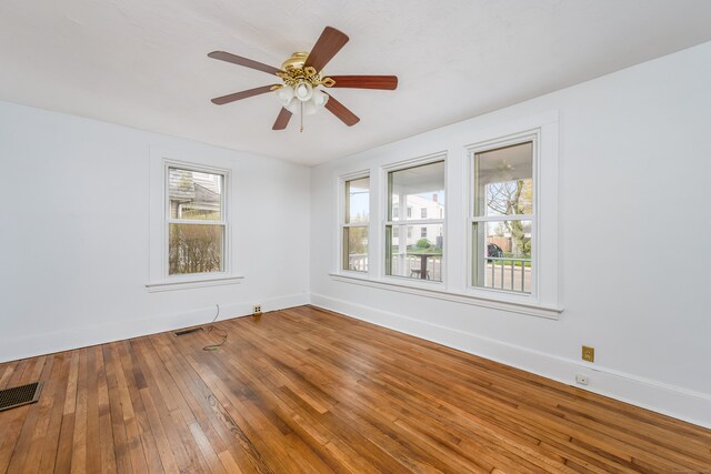 spare room with wood-type flooring, visible vents, a ceiling fan, and baseboards