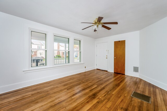empty room featuring hardwood / wood-style flooring, baseboards, a ceiling fan, and visible vents