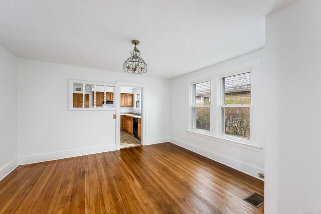 unfurnished dining area featuring wood-type flooring, a chandelier, visible vents, and baseboards