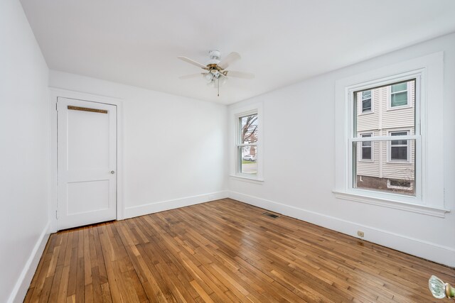 unfurnished room featuring baseboards, hardwood / wood-style flooring, visible vents, and ceiling fan