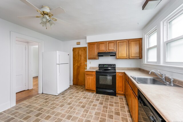 kitchen with a sink, black / electric stove, under cabinet range hood, dishwashing machine, and freestanding refrigerator