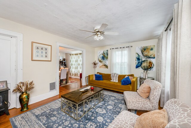 living area with baseboards, visible vents, a ceiling fan, wood finished floors, and a wood stove