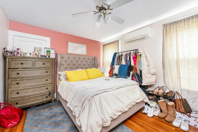bedroom featuring a wall mounted air conditioner, dark wood finished floors, and a ceiling fan