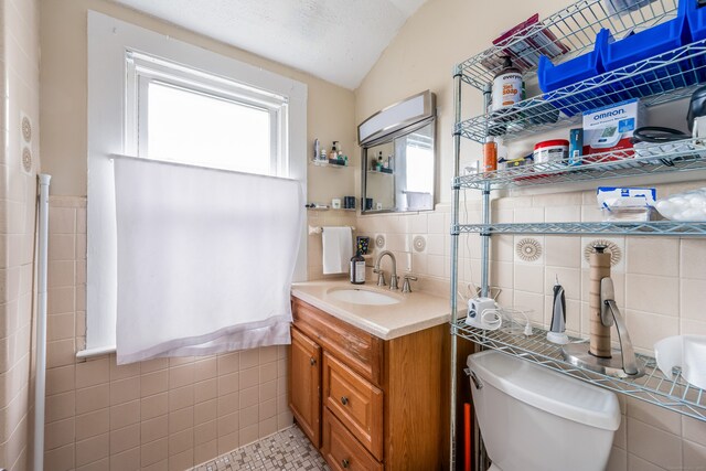 bathroom featuring lofted ceiling, toilet, vanity, and tile walls