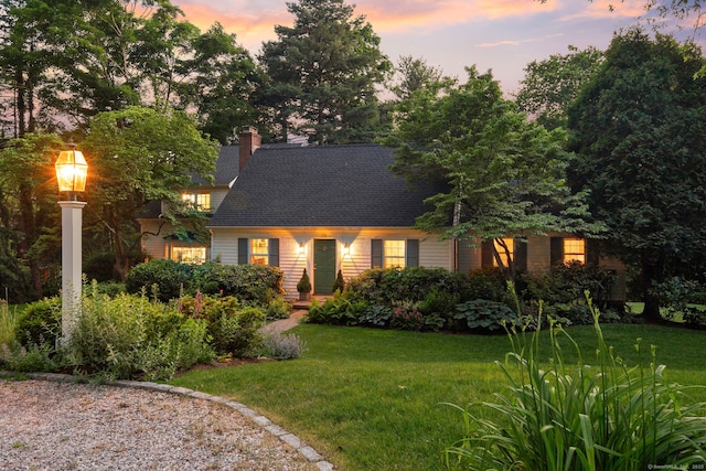 cape cod-style house featuring a lawn, a chimney, and a shingled roof