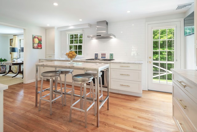 kitchen featuring visible vents, backsplash, white cabinets, and wall chimney range hood