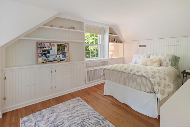 bedroom with radiator heating unit, wood finished floors, and vaulted ceiling