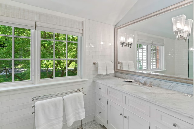 bathroom with lofted ceiling, vanity, a notable chandelier, and tile walls