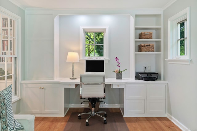 office area with light wood-style flooring, ornamental molding, and built in desk