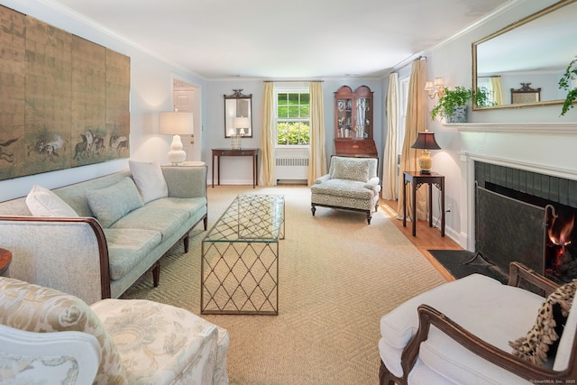 living area featuring a tiled fireplace, wood finished floors, radiator, baseboards, and crown molding