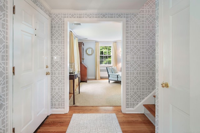 foyer entrance with wallpapered walls, ornamental molding, light wood finished floors, baseboards, and visible vents