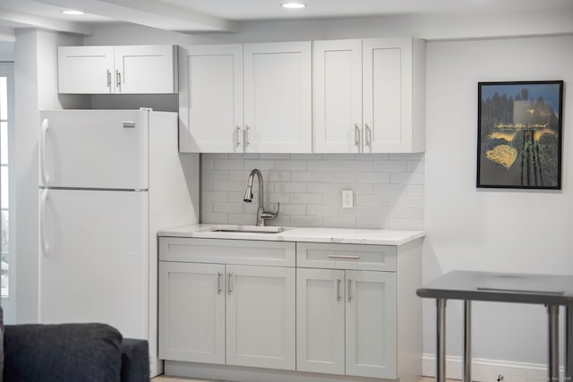 kitchen with recessed lighting, a sink, tasteful backsplash, light stone counters, and freestanding refrigerator