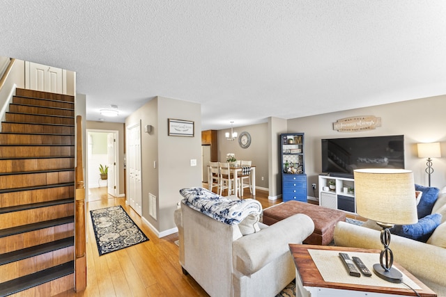 living room featuring stairs, light wood-style flooring, a chandelier, baseboards, and a textured ceiling