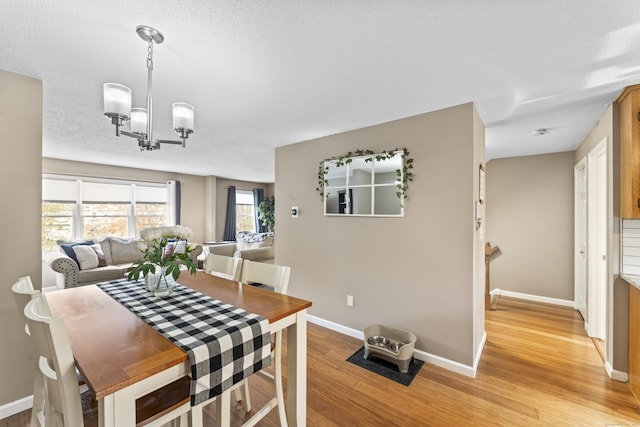 dining area with a textured ceiling, a chandelier, light wood finished floors, and baseboards