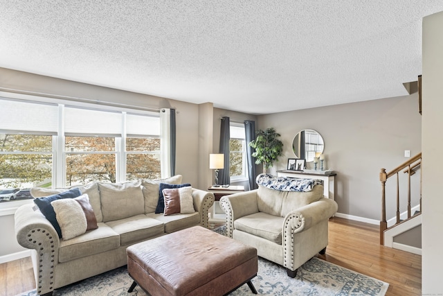 living room with baseboards, light wood-type flooring, a textured ceiling, and stairway