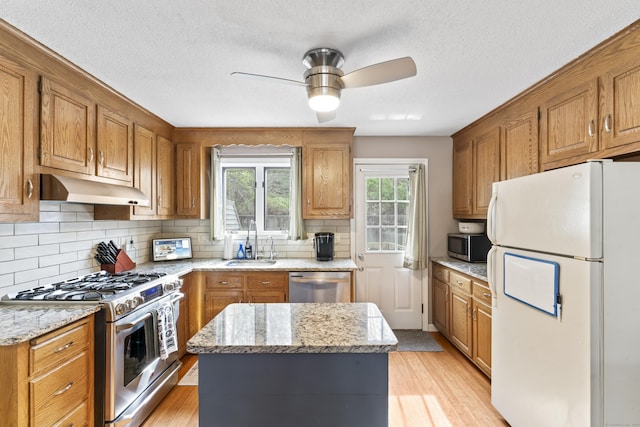 kitchen with a sink, stainless steel appliances, under cabinet range hood, a ceiling fan, and backsplash