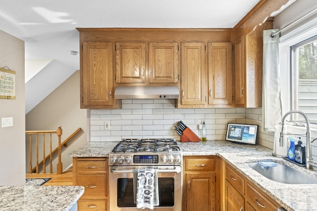 kitchen with exhaust hood, light stone counters, decorative backsplash, a sink, and stainless steel gas range