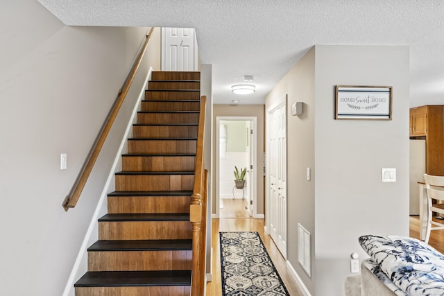 stairway featuring visible vents, wood finished floors, and a textured ceiling