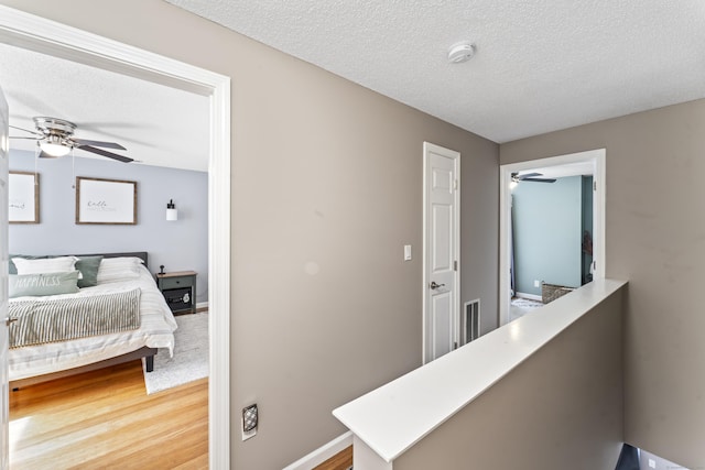 corridor with light wood-style floors, baseboards, visible vents, and a textured ceiling
