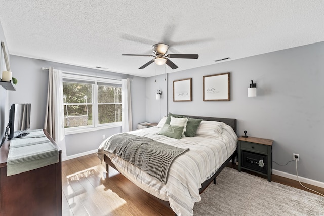 bedroom featuring baseboards, visible vents, wood finished floors, and a textured ceiling