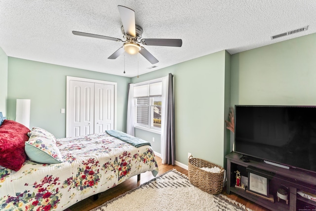 bedroom featuring wood finished floors, visible vents, a textured ceiling, and a closet