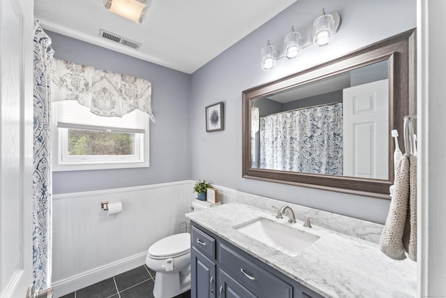 full bathroom featuring tile patterned flooring, wainscoting, toilet, vanity, and visible vents