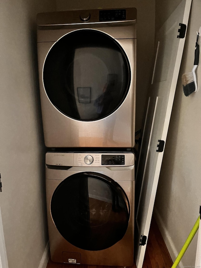 clothes washing area featuring stacked washer and dryer, laundry area, baseboards, and wood finished floors