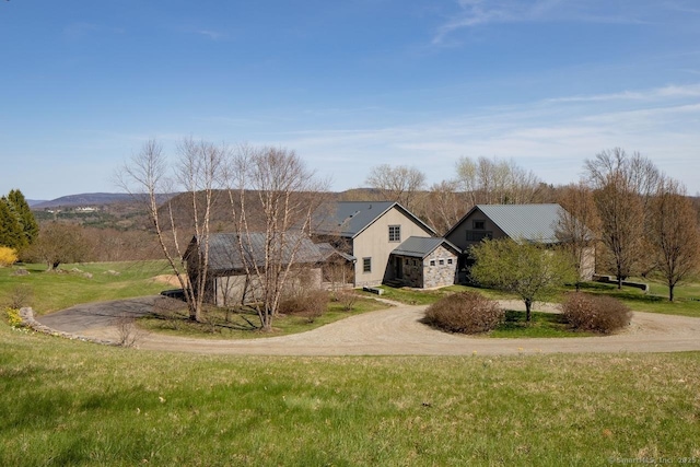 view of front of property featuring curved driveway, a front yard, metal roof, and stone siding