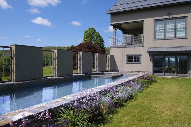 rear view of house featuring a standing seam roof, a balcony, metal roof, a yard, and an outdoor pool