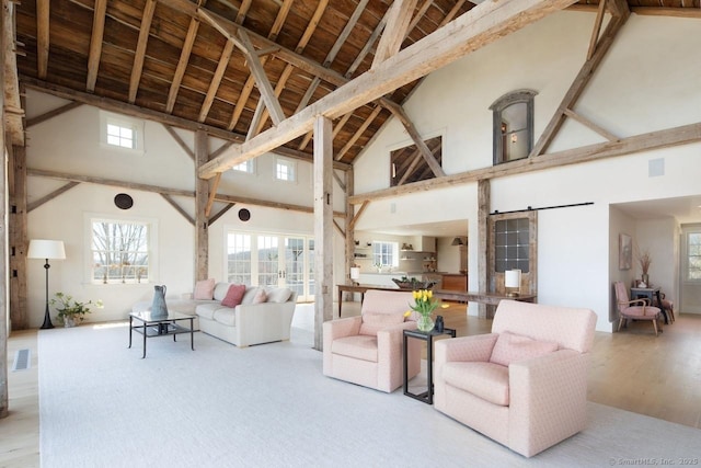 living room featuring a barn door, high vaulted ceiling, visible vents, and a wealth of natural light