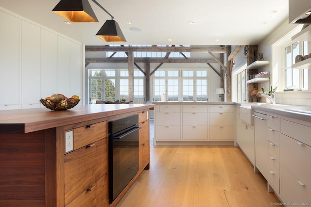 kitchen featuring decorative light fixtures, oven, light wood finished floors, a sink, and white cabinetry