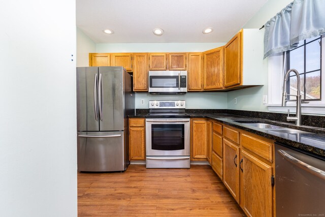 kitchen with dark stone countertops, light wood-style flooring, a sink, appliances with stainless steel finishes, and recessed lighting