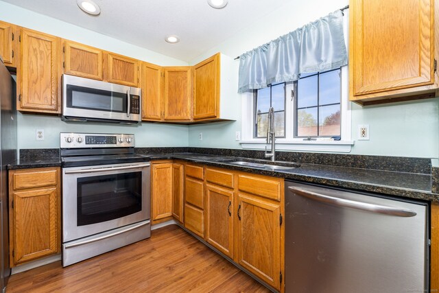 kitchen with dark stone countertops, recessed lighting, wood finished floors, appliances with stainless steel finishes, and a sink