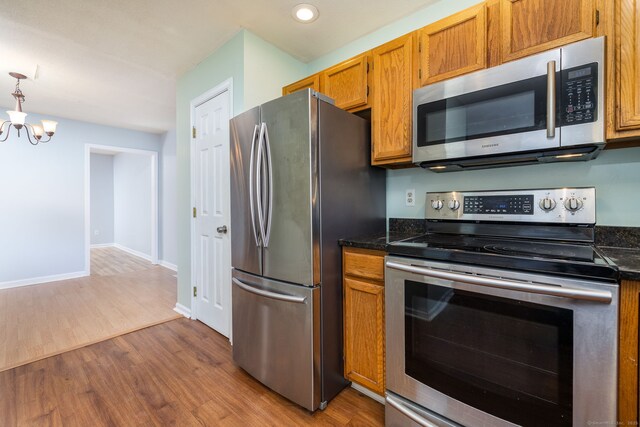 kitchen featuring an inviting chandelier, brown cabinetry, baseboards, appliances with stainless steel finishes, and wood finished floors