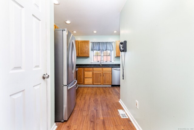 kitchen featuring dark countertops, stainless steel appliances, recessed lighting, wood finished floors, and brown cabinetry