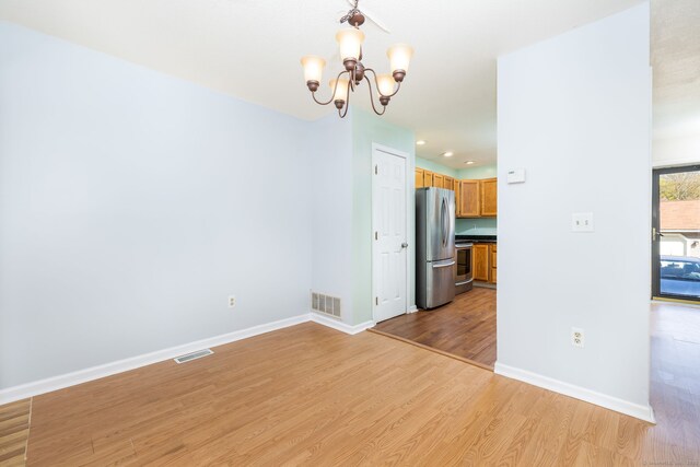 spare room featuring a notable chandelier, visible vents, baseboards, and light wood-style floors