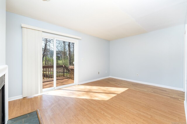 unfurnished living room featuring a fireplace with flush hearth, wood finished floors, and baseboards