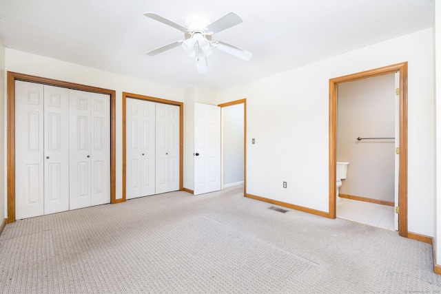 unfurnished bedroom featuring two closets, a ceiling fan, light carpet, baseboards, and ensuite bathroom