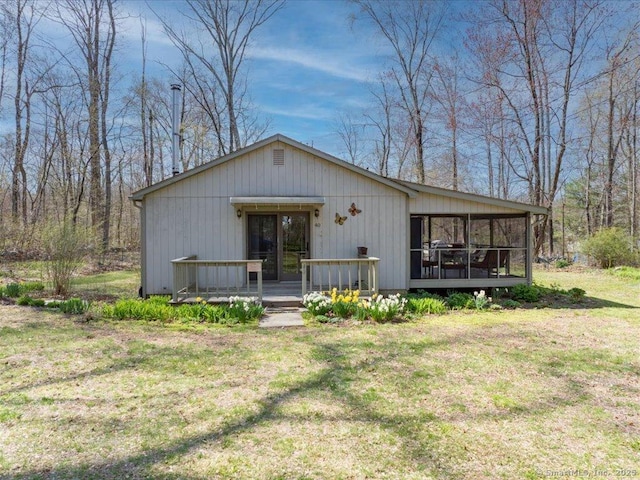 rear view of property featuring a deck, a sunroom, and a lawn