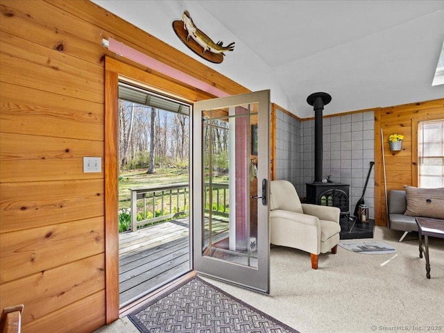 entryway featuring lofted ceiling, wooden walls, carpet flooring, and a wood stove