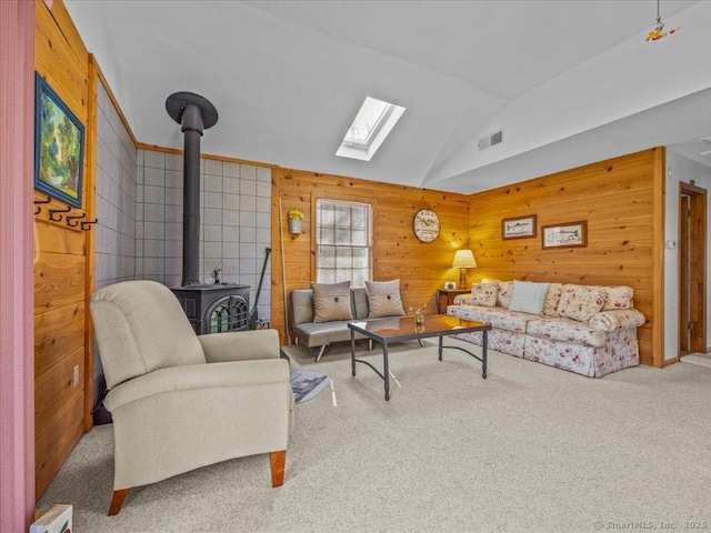 living area featuring a wood stove, carpet flooring, vaulted ceiling with skylight, and wood walls